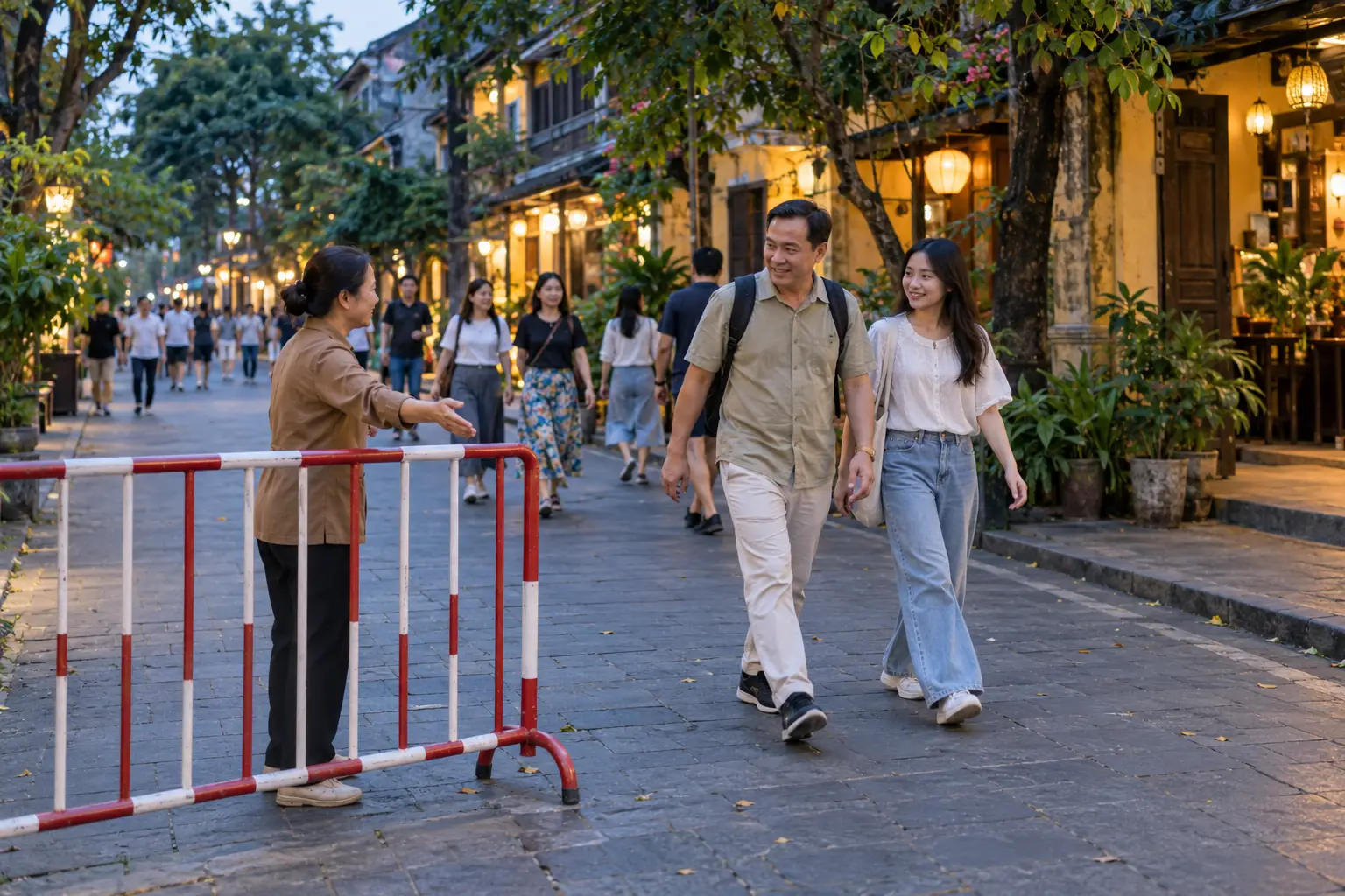 Hai người đi bộ qua lối cạnh rào chắn, một phụ nữ đưa tay hướng dẫn giữa con phố có nhiều người tản bộ lúc chạng vạng.