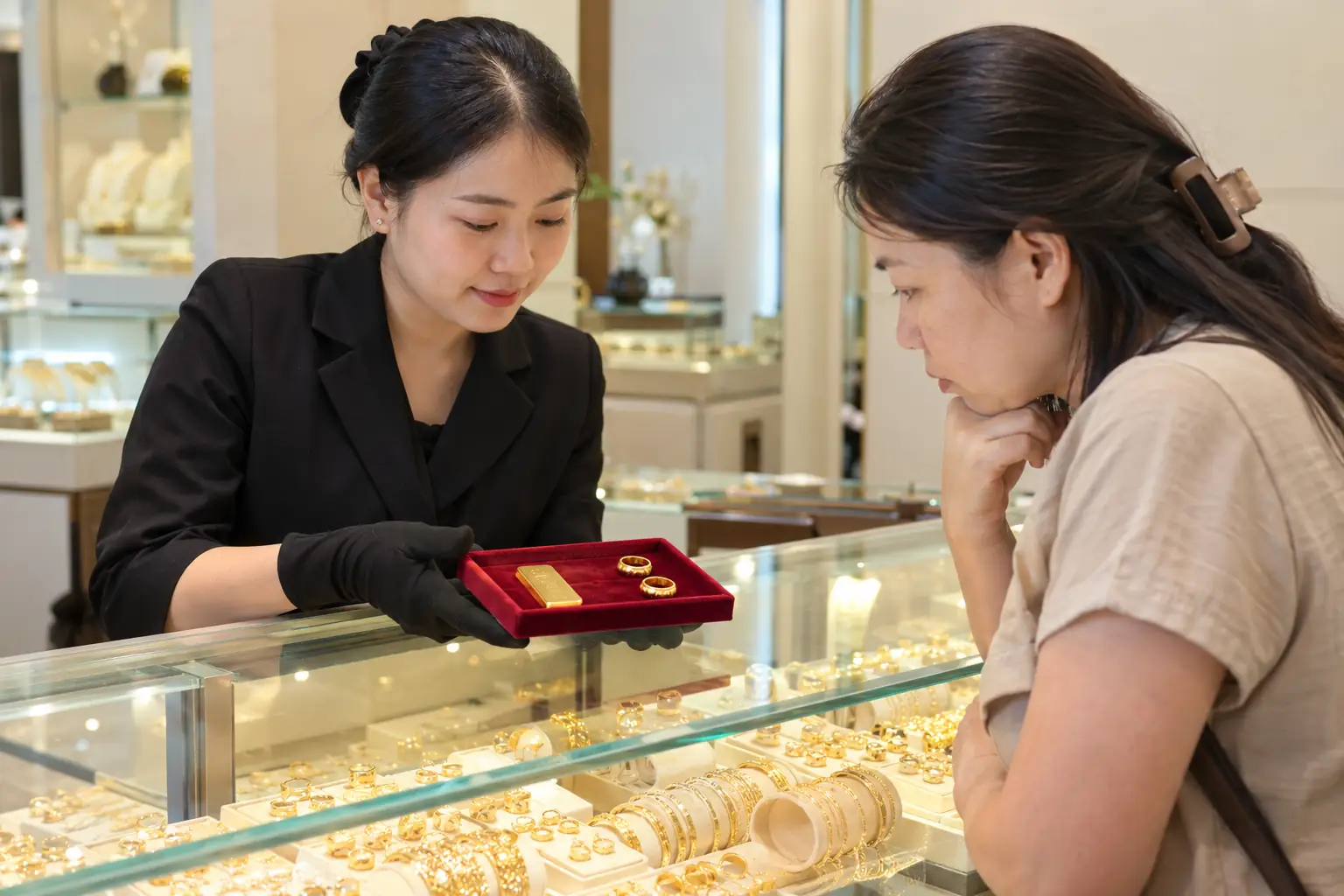 Nhân viên tiệm vàng đưa khay có vàng miếng và hai chiếc nhẫn để khách hàng xem tại quầy kính.