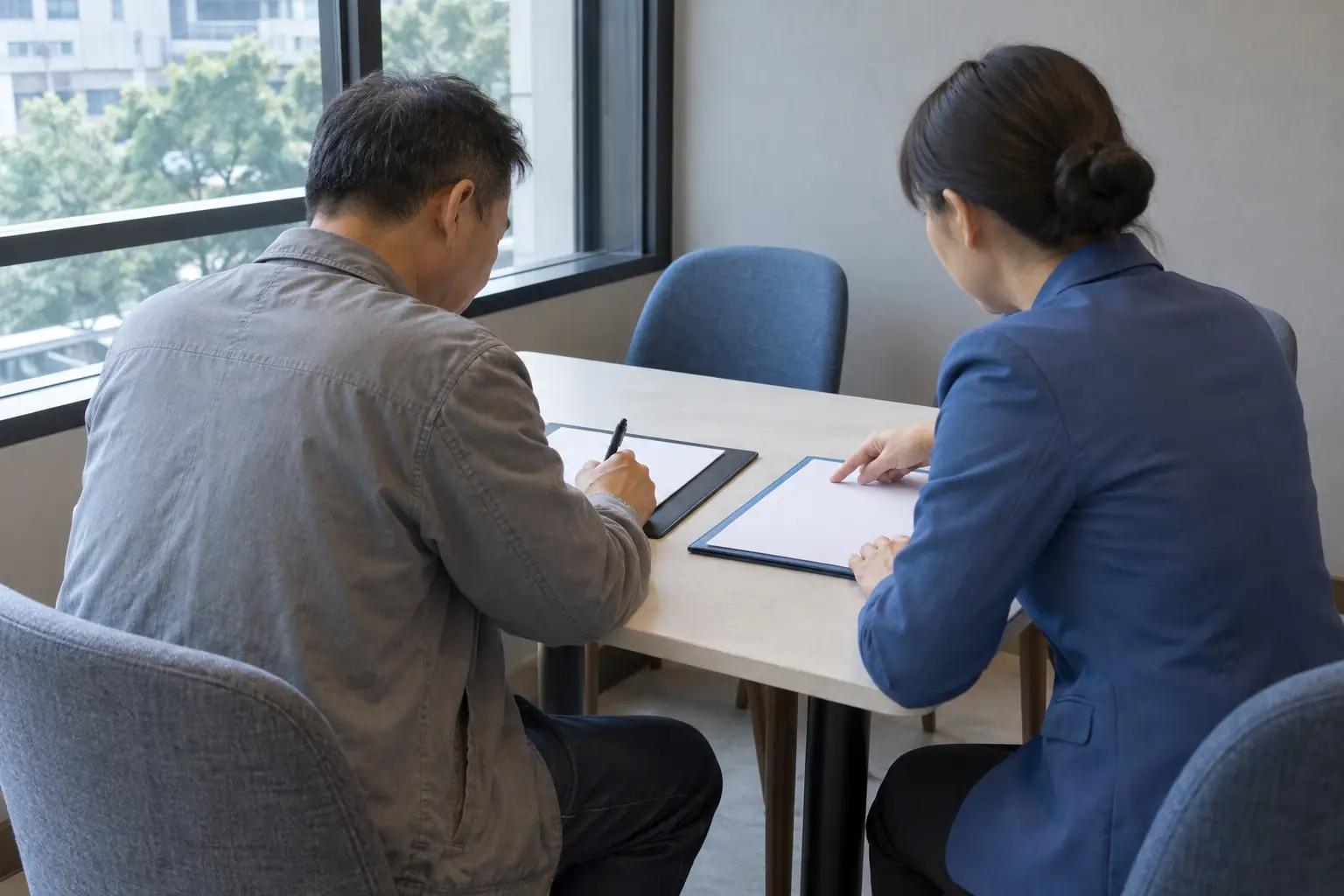 Ảnh minh họa AI: người đàn ông cầm bút trên giấy, cạnh người phụ nữ chỉ vào tập hồ sơ riêng tại bàn bên cửa sổ.