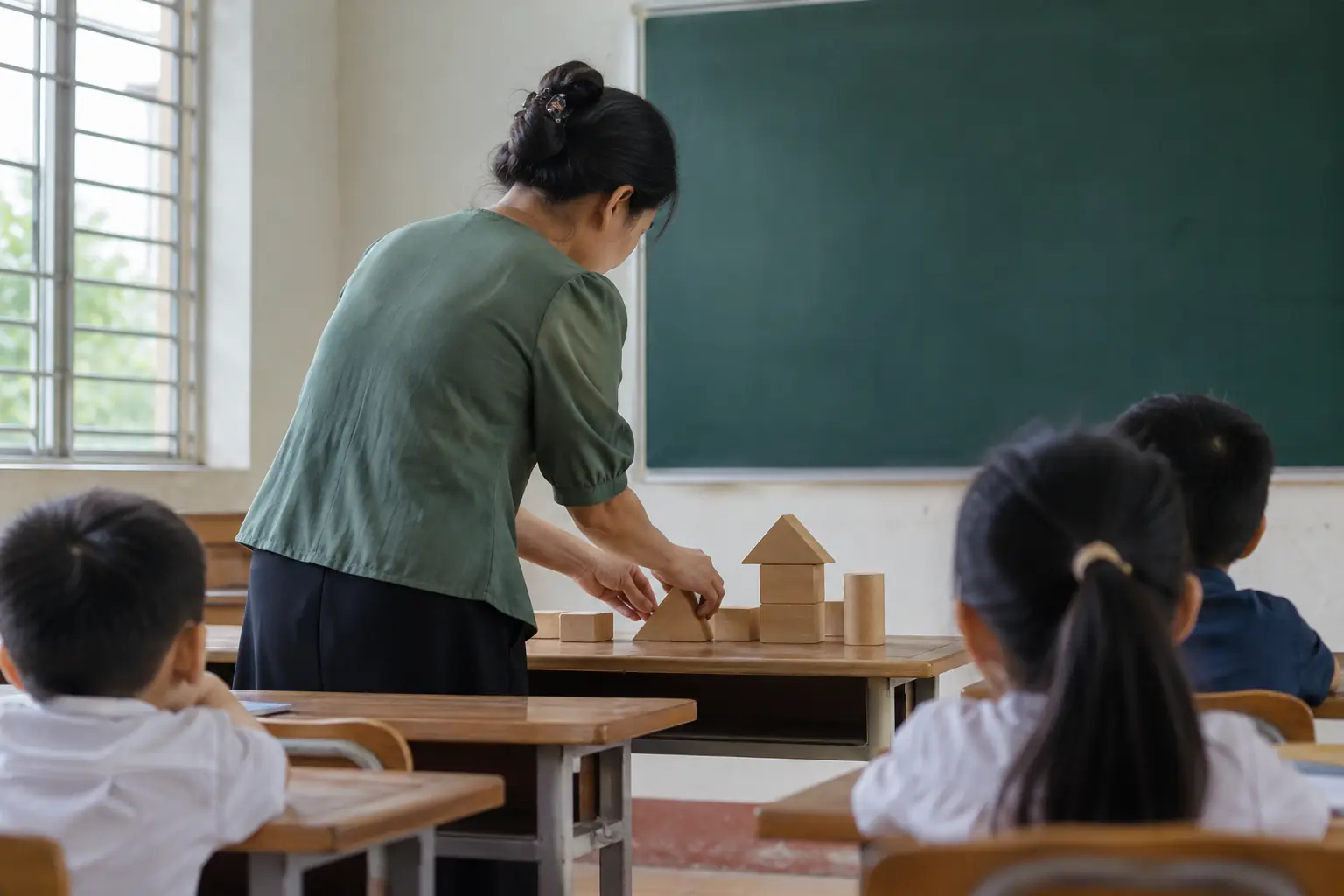 Ảnh minh họa AI: một giáo viên nhìn từ phía sau đang xếp các khối gỗ hình học trước những học sinh ngồi trong lớp.